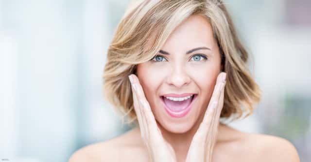 Smiling woman with hands in a V shape on either side of face (model)
