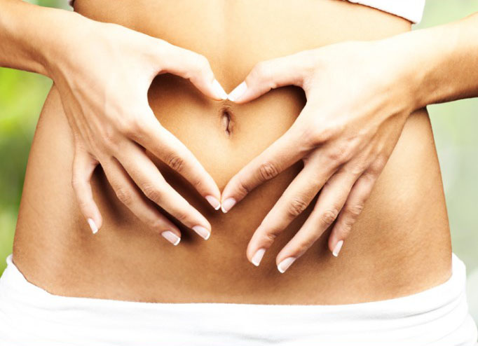 Woman's hands forming heart shape on bare abdomen