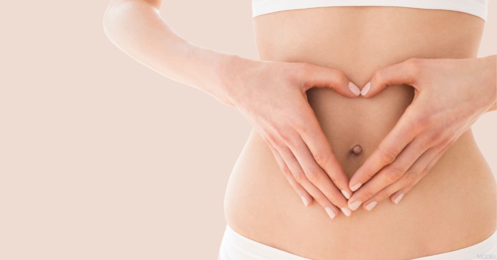 Woman's hands forming heart symbol over flat abdomen (MODEL)