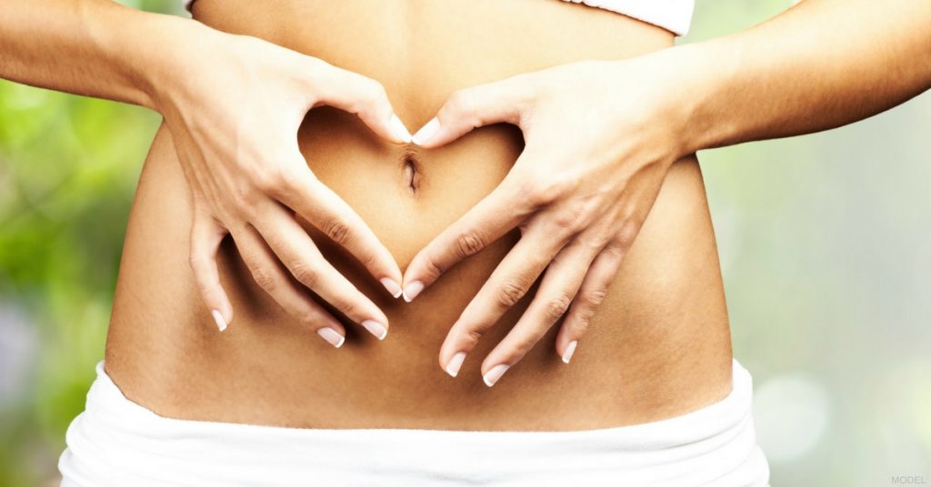 Woman's hands forming heart symbol over flat abdomen