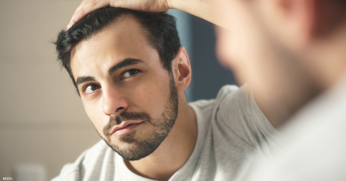 Man looking at receding hairline in the mirror