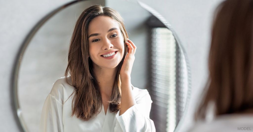 Women with beautiful skin smiling at her reflection in the mirror (model)