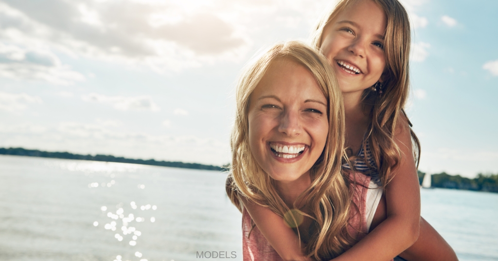 Glowing mother with daughter piggyback at the beach (models)