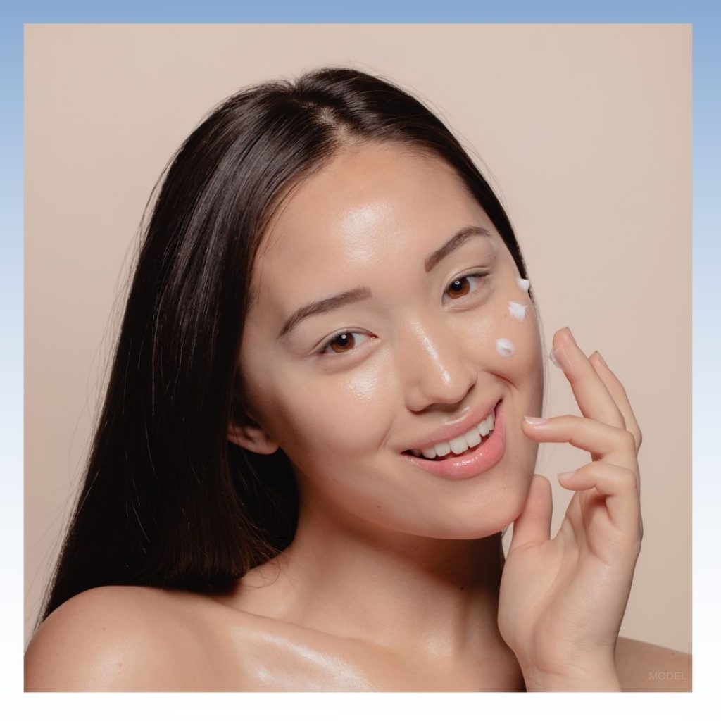 Smiling woman with skincare on her cheek and her hand held up by her face (model)